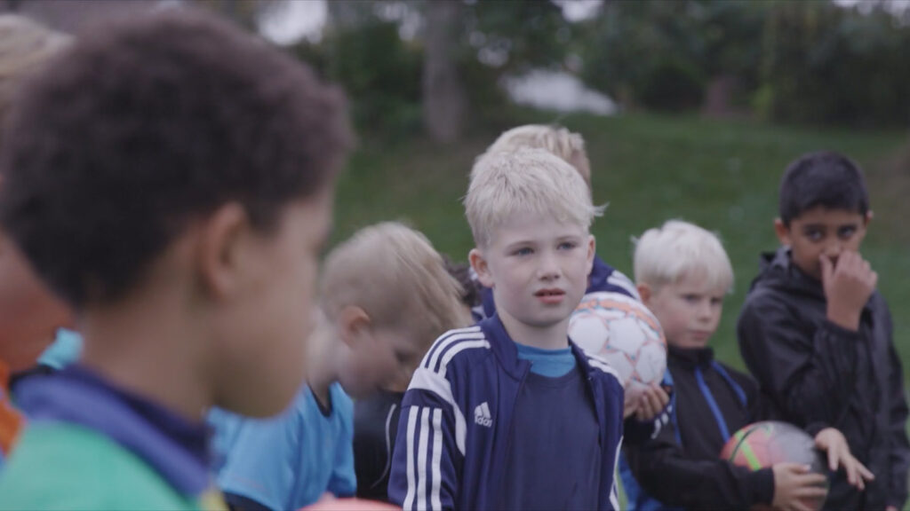 Bilde av gutter på fotballbane, gutten Sondre ser bekymret rett på deg fordi han skal hjem til en mor som drikker for mye alkohol