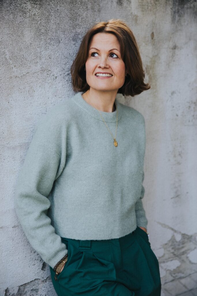 Dr. Marianne Natvik i mintgrønn genser, foran en grå murvegg. Ser seg til siden og smiler.